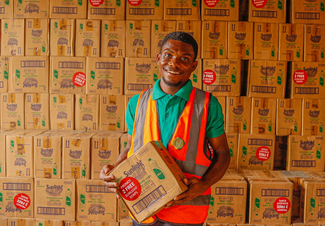 Warehouse employee holding a box while smiling in a stockroom filled with Sunlight boxes.